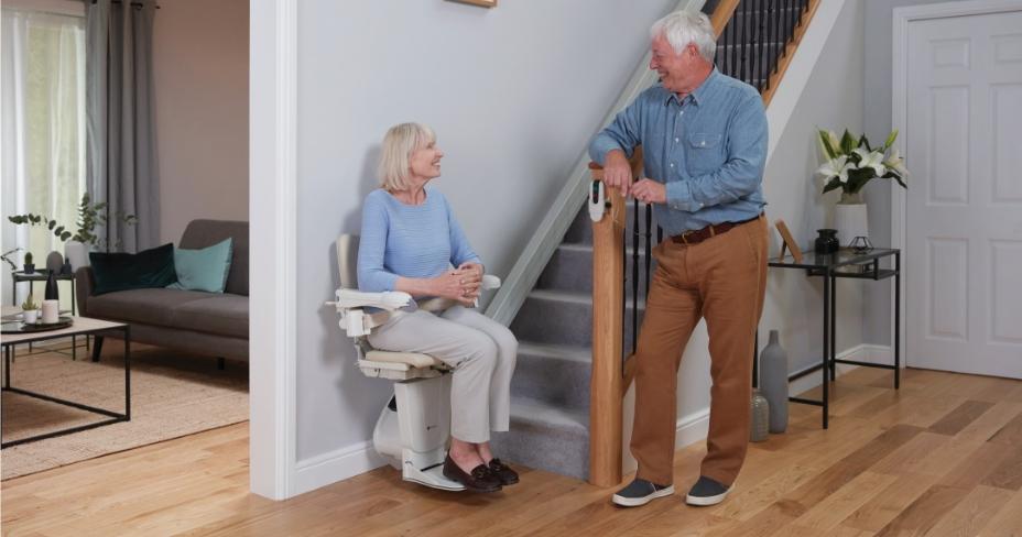 women and man at bottom of stairs talking. Lady sat in stairlift